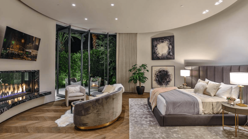 living-in-luxury-home-decor-trends-2021 Large plush bed and couch facing a large mounted TV and a modern fireplace