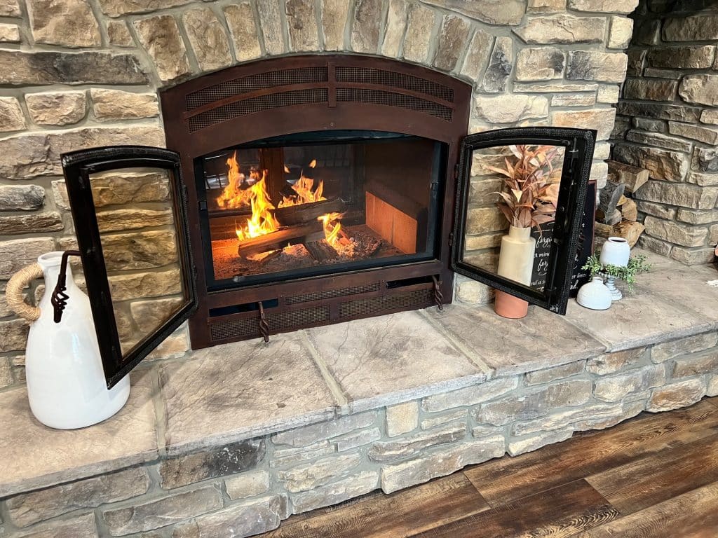 A standard wood-burning fireplace with its doors open, creating a warm, open-hearth ambiance in a traditional living room.