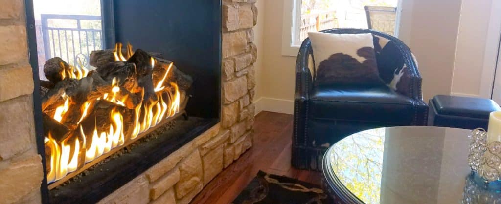 an image of a gas fireplace with logs that has an indoor side and outdoor side