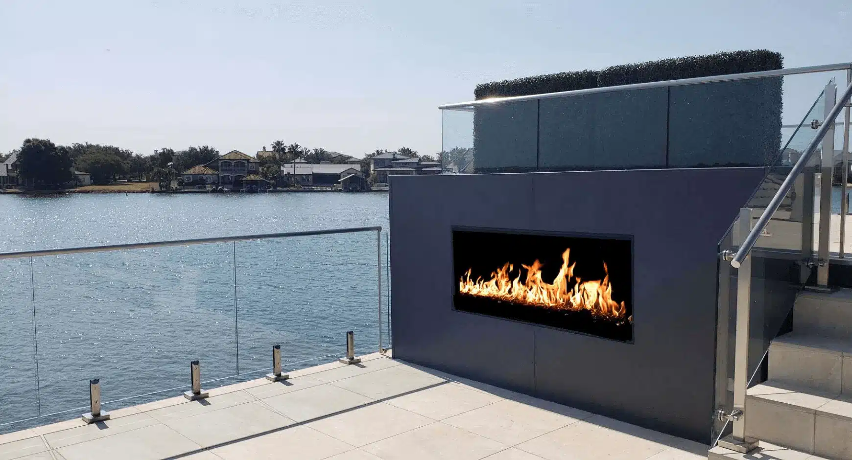 Acucraft custom outdoor linear gas fireplace installed on a waterfront patio, adding modern elegance and radiant flames to a luxurious outdoor living space.