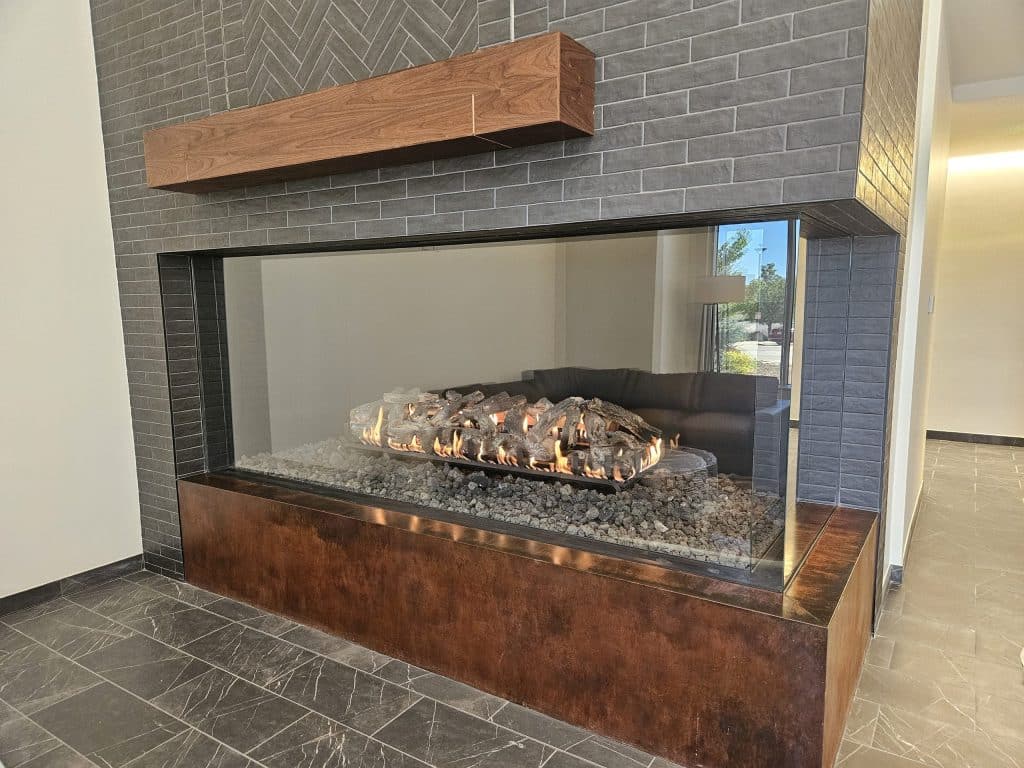 Acucraft Custom Front & Right Side Gas Fireplace with Logs (1) Sleek corner-view fireplace dividing living spaces with contemporary stone and glass design