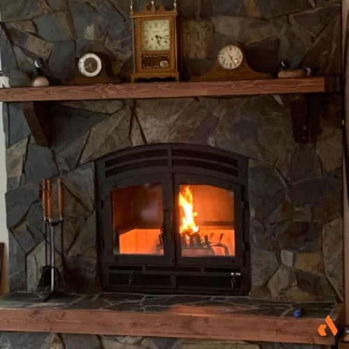 an image of a rustic wood burning fireplace with stone surround and wood mantel and hearth