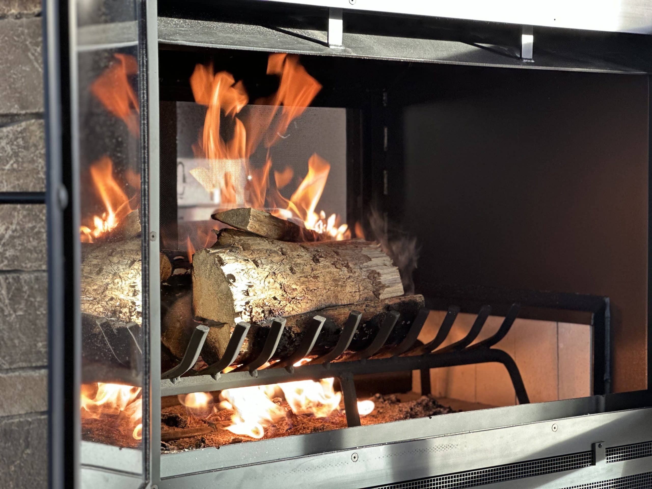 Close-up of burning logs inside an Acucraft Hearthroom 44 see-through wood fireplace, showcasing a vibrant fire with a rectangular finish and spring handles.